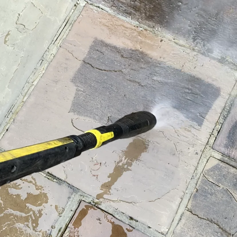 A pressure-washing lance clearing surface dirt from paving